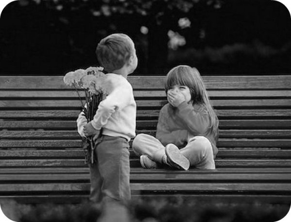 Мальчик дарит цветы девочке на скамейке