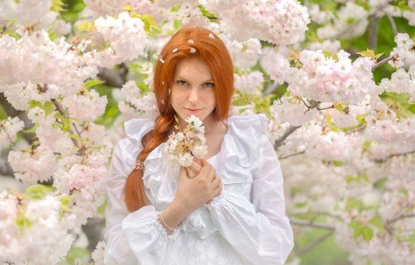 Рыжая девушка у цветущих деревьев