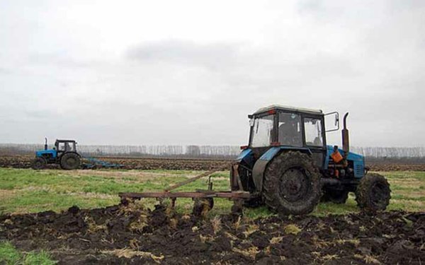 Трактор в поле пашет землю