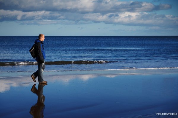 Человек идет по берегу моря