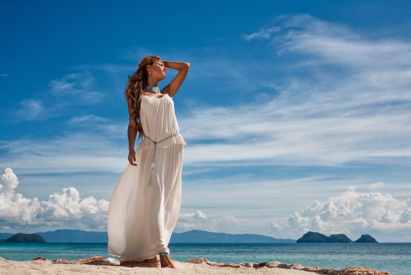 Красивая молодая женщина в белом платье и соломенной шляпе с видом на море