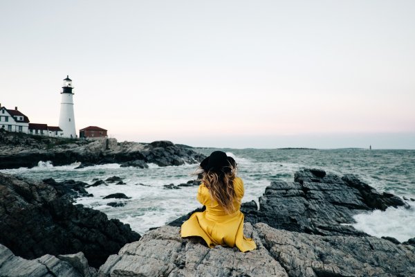 Девушка сидит на скале у моря