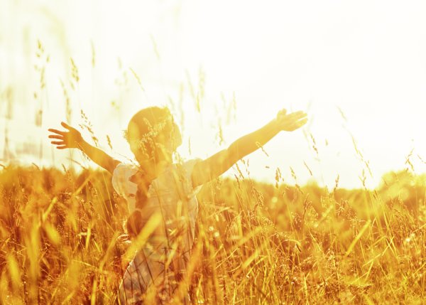 Маленькая девочка поднимает руки к солнцу