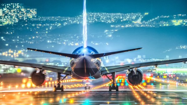 Бизнесмен в аэропорту смотрит на взлетающий самолет на фоне заката