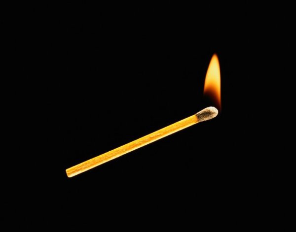 Зажженная спичка на белом фоне