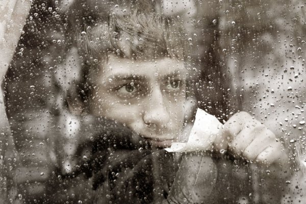 Человек грустит у окна в дождь