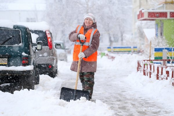 Убирает снег возле машины