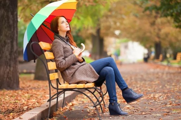 Девушка сидит на скамейке в парке осенью